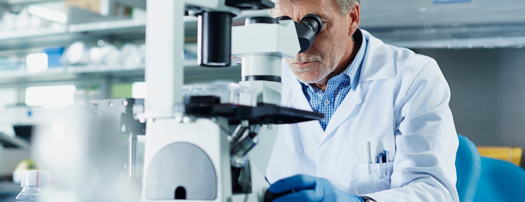 A man in a lab coat examines a sample through a microscope in a laboratory setting.