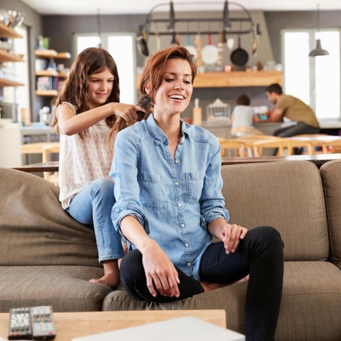 Daughter Braids Mother's Hair As They Sit On Sofa